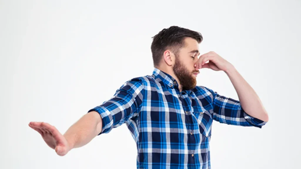 Man in a plaid shirt pinching his nose and holding his arm out, reacting negatively as if rejecting a bad smell or unwanted situation.