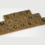 Scrabble tiles spell 'STOP MAKING EXCUSES' on a light surface.