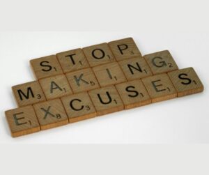 Scrabble tiles spell 'STOP MAKING EXCUSES' on a light surface.