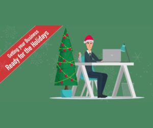 Illustration of a person in a Santa hat at a desk with a laptop, a Christmas tree nearby, and a red banner reading Getting your Business Ready for the Holidays.